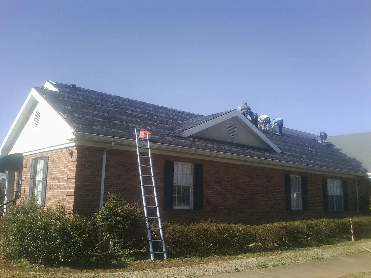Crew tearing shingles off a brick ranch roof with a ladder set — Emergency Roof Repair work by our crew in Felicity