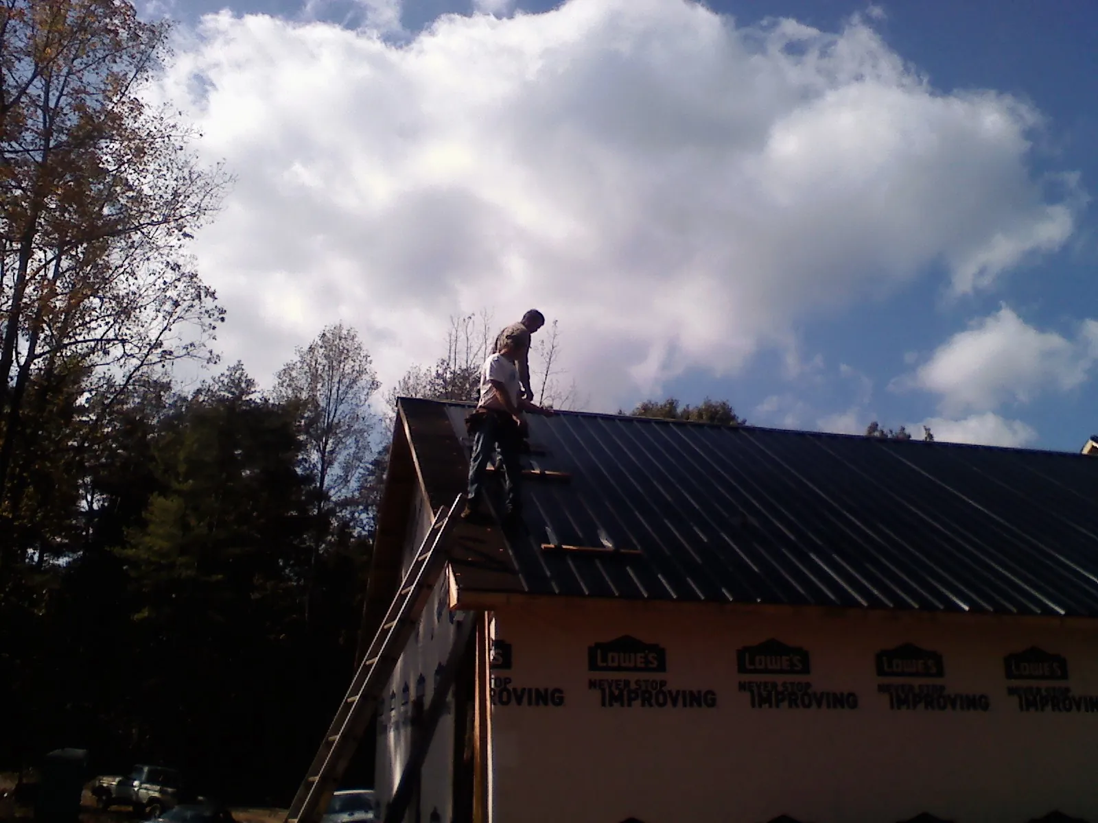 Roofer fastening dark metal panels high against a cloudy sky, from a Roof Inspection job in Felicity