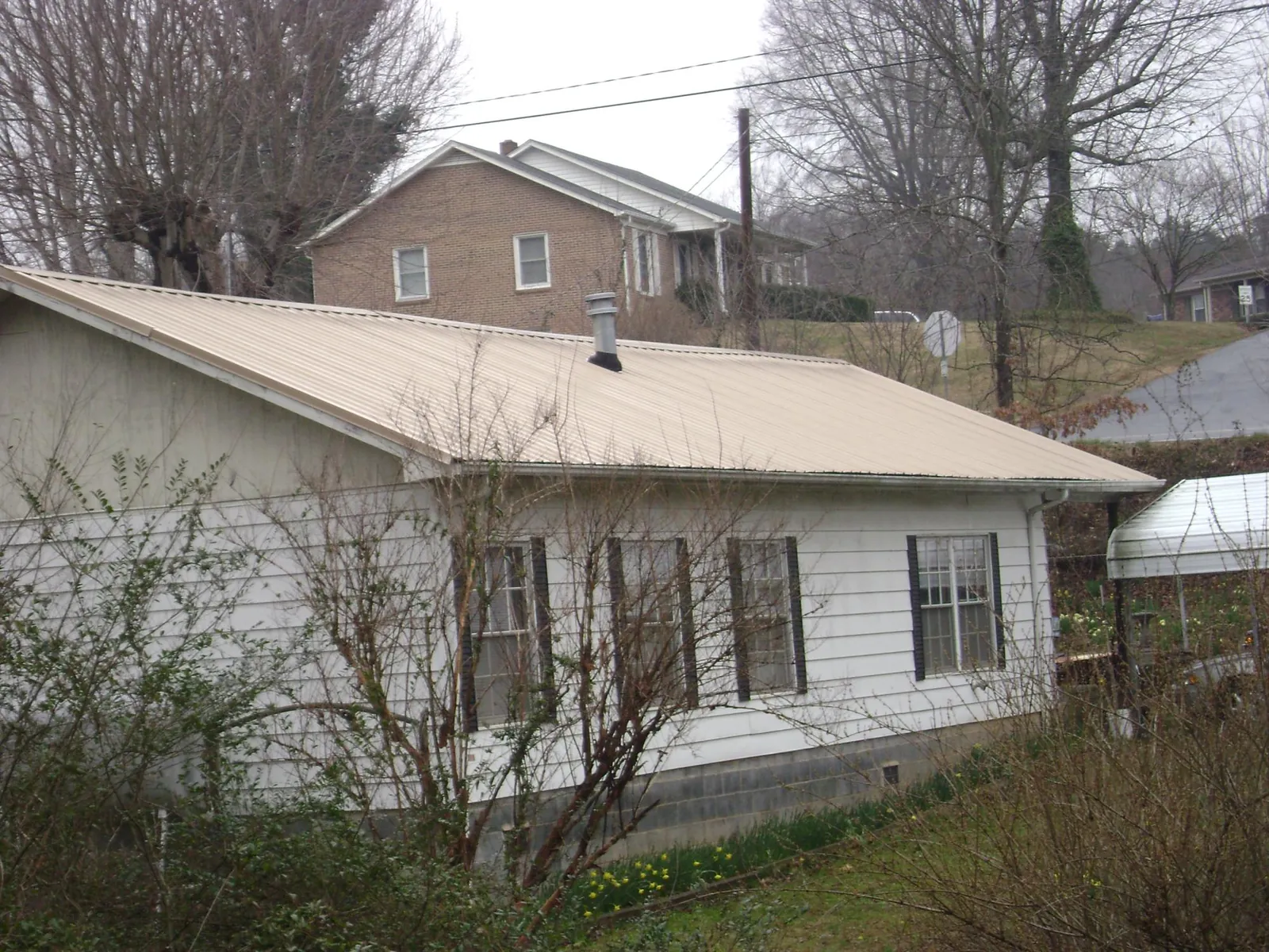 Tan metal roof on a white sided house set into a hillside — Commercial Roofing by Roofing Brothers in Felicity